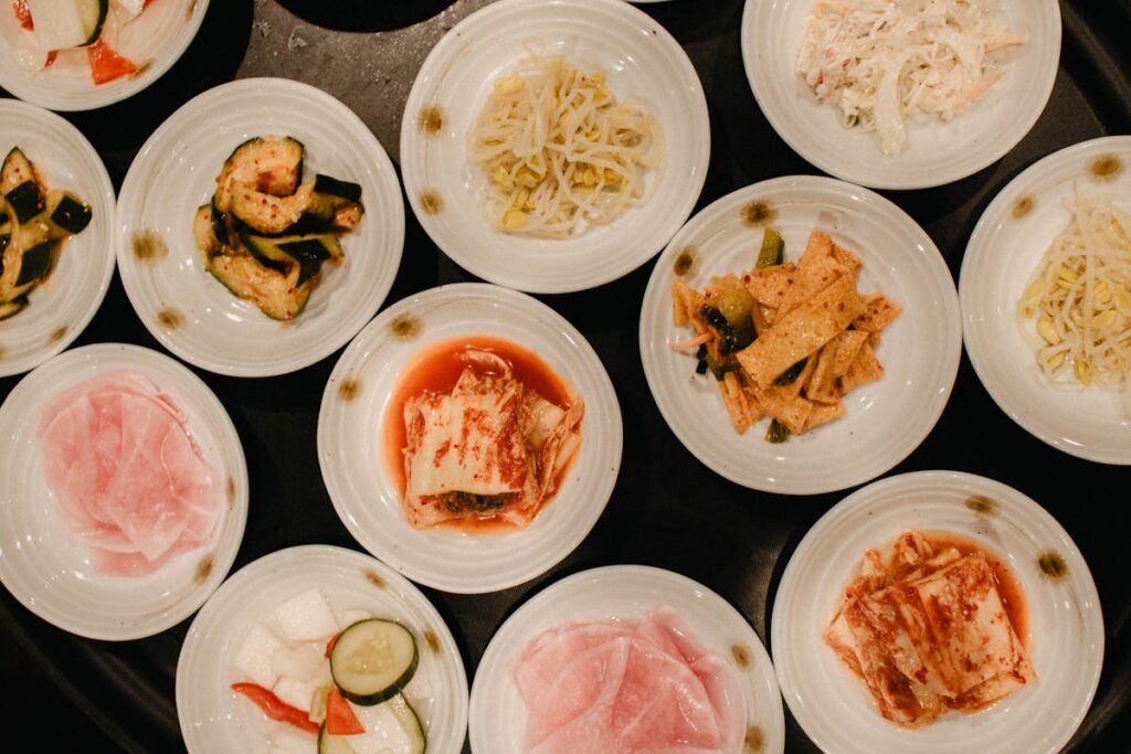 An overhead view of various Korean side dishes served in white bowls.
